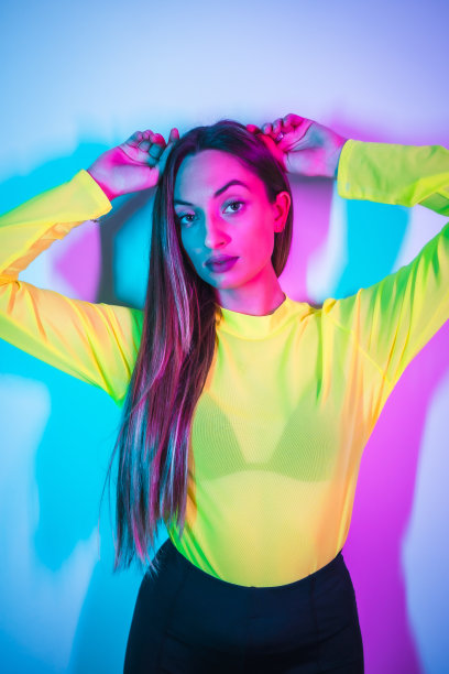 派对生活在夜总会与粉红色的蓝色霓虹灯，一个年轻的金发白人女孩在黄色t恤的肖像图片下载