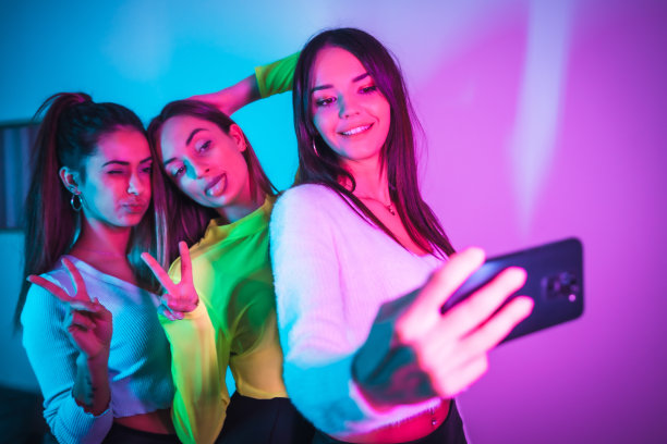 朋友们的生活方式在一个迪斯科舞厅与蓝色和粉红色的霓虹灯，有乐趣地拍照与手机的社交网络图片下载