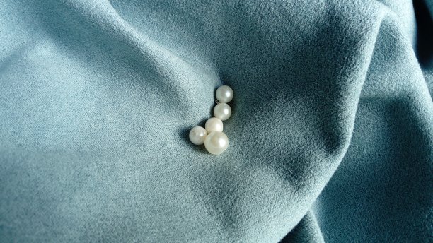 白色的珠子散落在蓝色天鹅绒织物上。窗帘上的珠宝。珍珠母的光泽和浅色在短绒上的美丽组合。织物上的褶皱和波浪图片下载