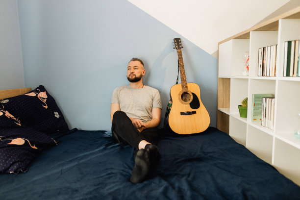 千禧一代的男人在家里的床上拿着原声吉他图片下载