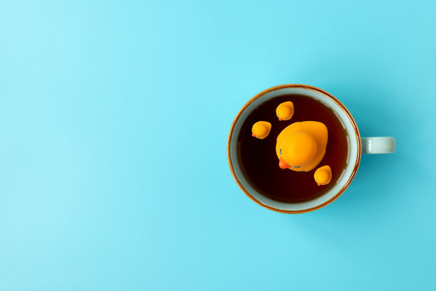 黄色的橡皮鸭家族游泳进杯茶在蓝色的背景。创意暑假概念。俯视图图片下载
