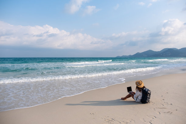 一位坐在海滩上使用笔记本电脑的女性旅行者图片下载