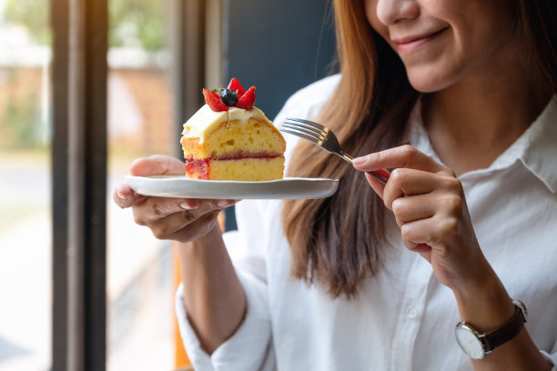 一个年轻美丽的亚洲女人拿着叉子吃蛋糕图片下载