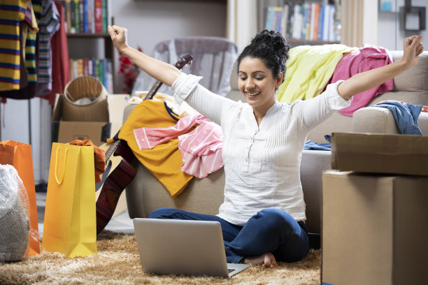 一个年轻女性庆祝她的胜利，她坐在家里的地毯上:-库存照片图片下载