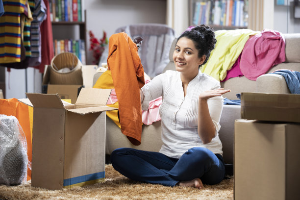 一个年轻女子展示衣服打开箱子，坐在家里的地板上的照片:库存照片图片下载