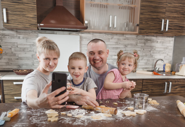 幸福的家庭，爸爸妈妈和两个孩子在厨房做饼干的时候自拍。一起做饭，幸福的家庭关系图片下载