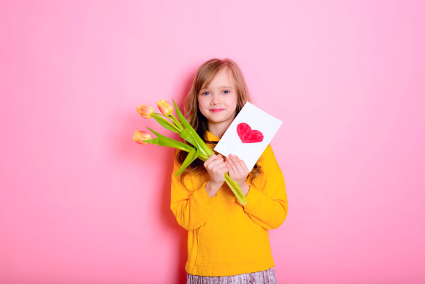 复活节快乐!金发小妞戴着兔耳朵，手里拿着一张卡片，红心，黄郁金香。母亲节快乐!国际妇女日。女儿的一天。图片下载