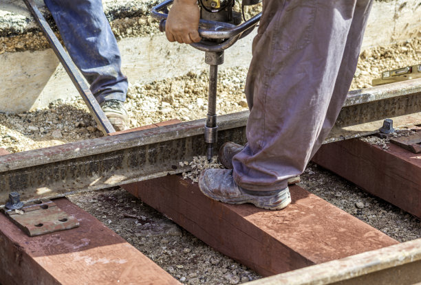 用木枕木建造铁路轨道。工人用钻头钻出一个孔，用来固定枕木上的轨道的螺栓将被固定住。图片下载