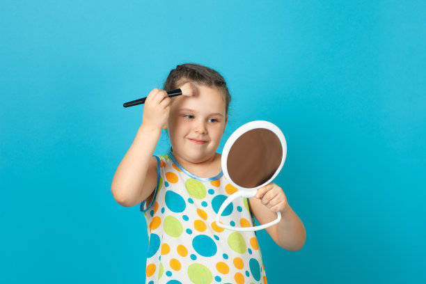 一个女孩的肖像在一个白色的夏季连衣裙粉她的额头与一个大刷子和做博主化妆，孤立在一个蓝色的背景图片下载