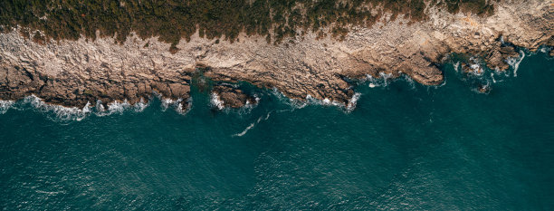 鸟瞰图的岩石海滩和大海与透明的蓝色水在日落。夏季日落时的亚得里亚海海岸。前视图。景观清澈蔚蓝的水，石头和岩石。自然背景图片下载