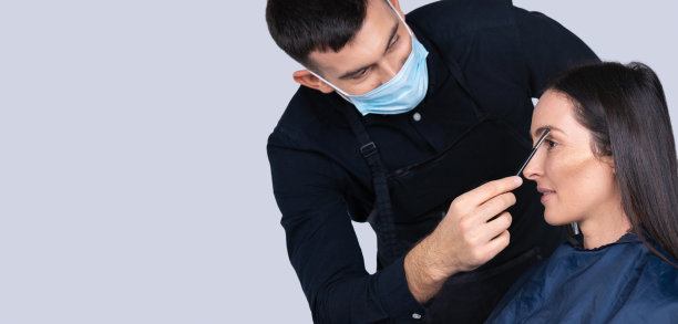 横幅,长格式。剪裁照片的男化妆师在医疗面具和黑发模特女孩。流行病期间的工作和美丽。图片下载