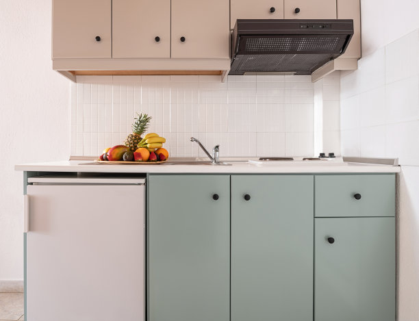 在现代室内厨房的简单橱柜模块的空墙上，白色瓷砖防溅板的特写，有小冰箱，通风口，水槽，炉子，水果盘图片下载