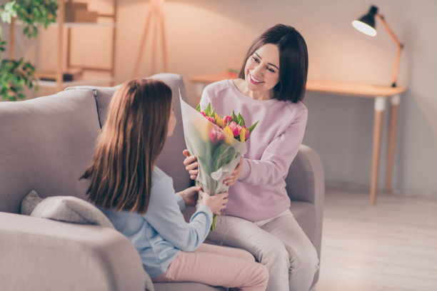 乐观的照片，黑发，红头发的妈妈，女儿，捧着花，坐在沙发上，穿毛衣裤子在家图片下载