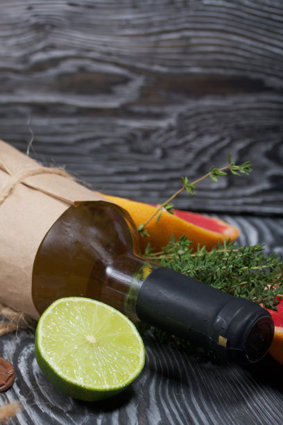 酒精瓶。包裹在纸上。旁边放着百里香，半块酸橙和葡萄柚。松木板。图片下载