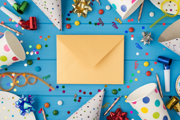 顶视图照片的生日聚会组成封闭的工艺纸信封在中间螺旋管，缎带，星星，蜡烛，烟斗，帽子，纸杯和盘子孤立的蓝色木制桌子的背景图片下载