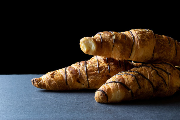 羊角面包的背景。法国早餐牛角面包，新鲜的糕点面包与巧克力在面包房的黑色石头背景。面包烘焙产品咖啡概念。图片下载