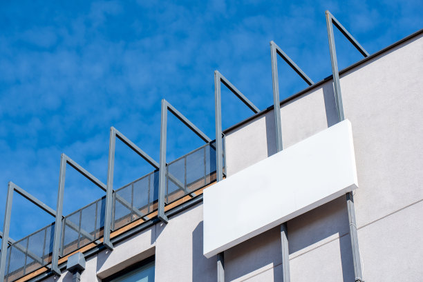 在阳光明媚的日子里，建筑正面的白色空白金属广告牌上有公司的标识图片下载