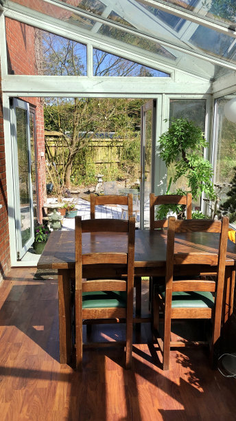 室内的玻璃温室，用餐区，深色木质餐桌和椅子，敞开的门可以看到家庭花园图片下载