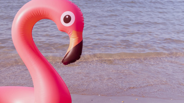 夏天有趣的海滩。粉红色的充气火烈鸟在蓝色的海水在夏季海洋海滩的背景。有趣的小鸟玩具的孩子。图片下载