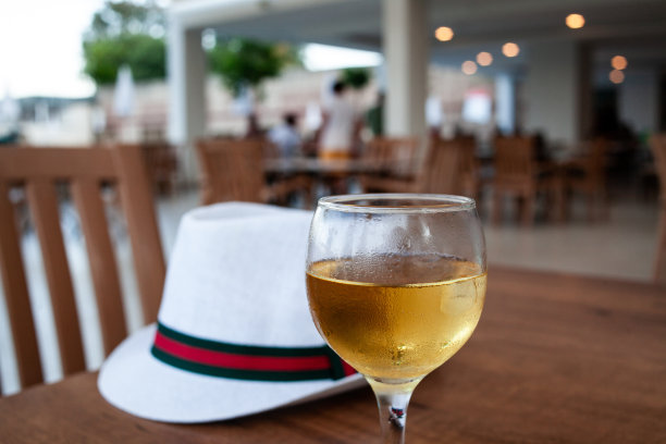 桌上放着一杯白葡萄酒和一顶白帽子。凝结在一杯清爽的葡萄酒上。露天餐厅的冷饮。放松与酒精图片下载