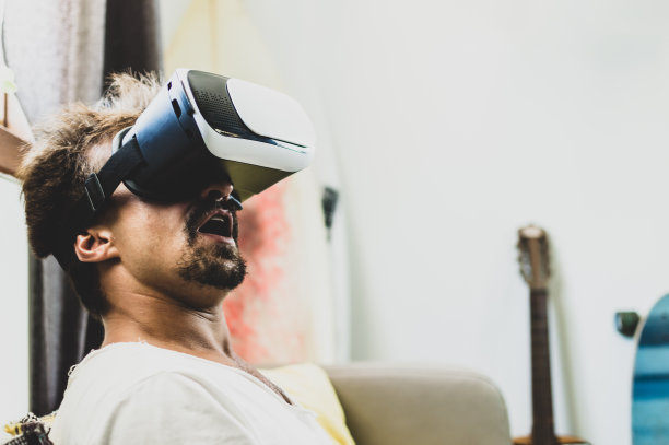 一个戴着虚拟现实眼镜坐在家里沙发上的男人图片下载