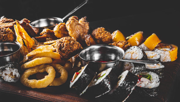 啤酒盘配辣鸡翅、薯条、炸洋葱圈、芝士球、寿司卷、面包屑、酱料放在木桌上图片下载