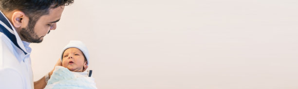 年轻亚裔印度父亲抱着新生儿的特写，留有文案空间。医疗保健和医疗托儿所关爱生活方式父子情深父亲节banner（模糊）图片下载