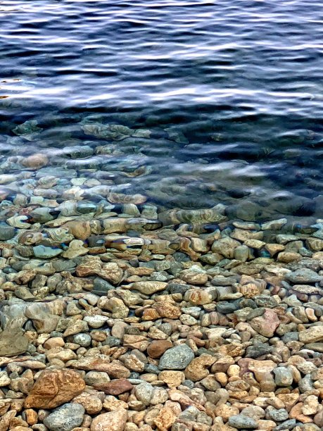 碧波荡漾的卵石滩背景，透明的碧波荡漾在卵石滩岸边。图片下载