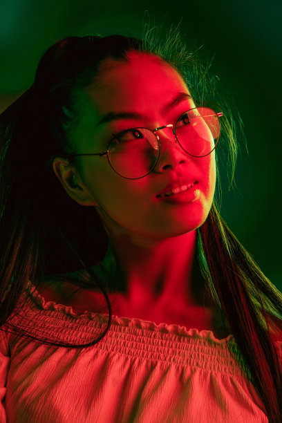 年轻美丽的亚洲女孩孤立在红绿色霓虹灯的背景。图片下载