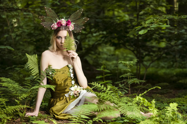 性感美丽的白人女性在绿色连衣裙装饰鲜花摆姿势在森林户外。水平的形象图片下载