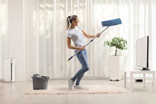 年轻女子坐在电视机前，一边打扫一边用拖把跳舞图片下载