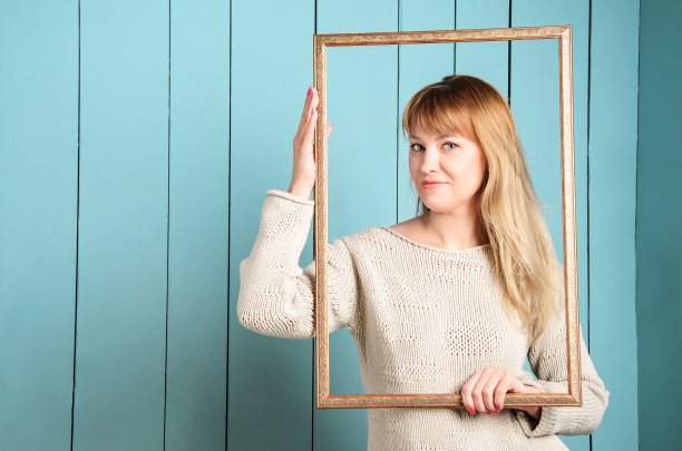 美丽漂亮的金发年轻女子与松散的头发持有古董木制相框和微笑图片下载