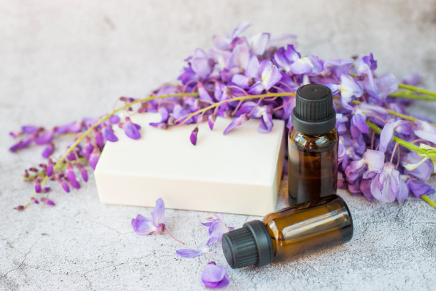 灰色的背景上是白色的肥皂、两罐天然油和鲜花。图片下载