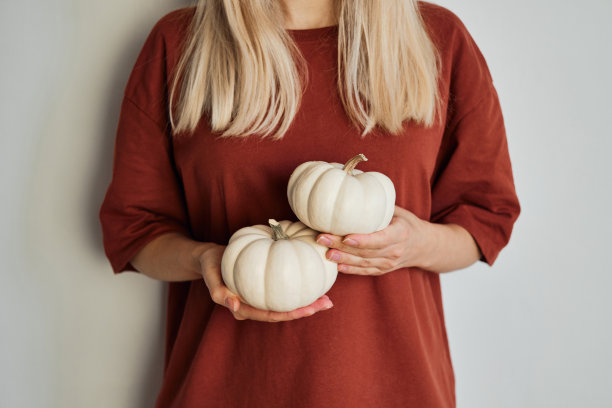 一个穿着红色t恤的女孩手里拿着南瓜。天然新鲜有机蔬菜。白南瓜特写。生食饮食健康。南瓜节、感恩节和万圣节。海报,横幅图片下载