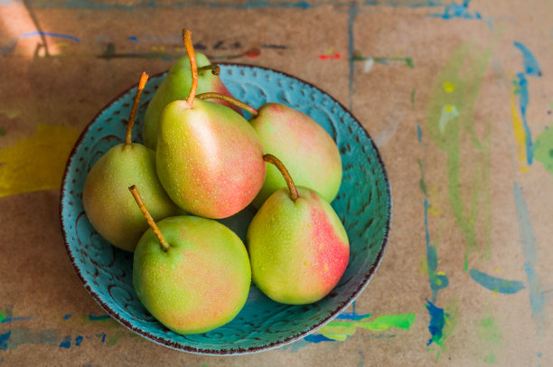 阳光下，一个绿松石色的盘子上放着一面红边的绿梨。图片下载
