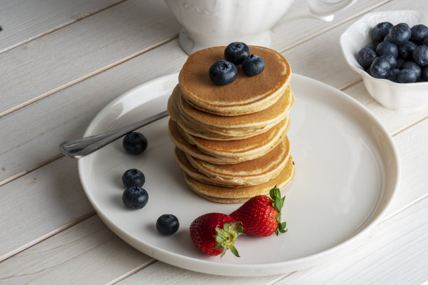特写美味的煎饼，与新鲜的蓝莓，草莓在一个白色的木头背景，煎饼库存照片图片下载