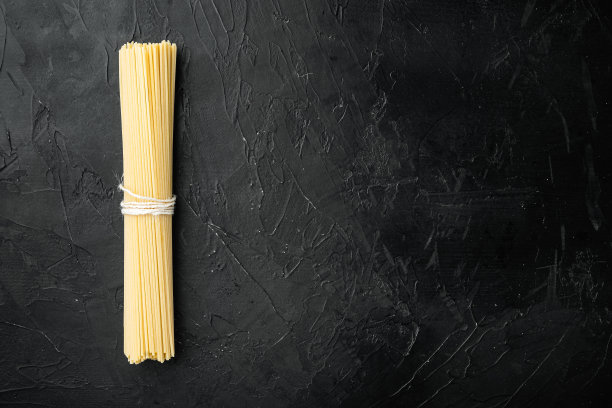 全麦意大利面，黄色长的生干意大利面，在黑色的石头背景上，俯视图平铺，有文字拷贝空间图片下载