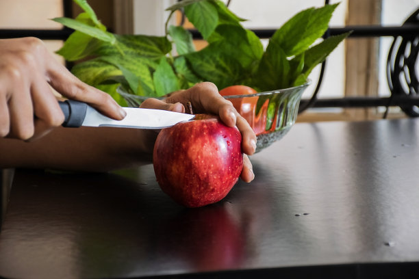 一个女人在早上切新鲜的红苹果作为早餐的库存照片，苹果保存在黑色的桌子上。图片下载