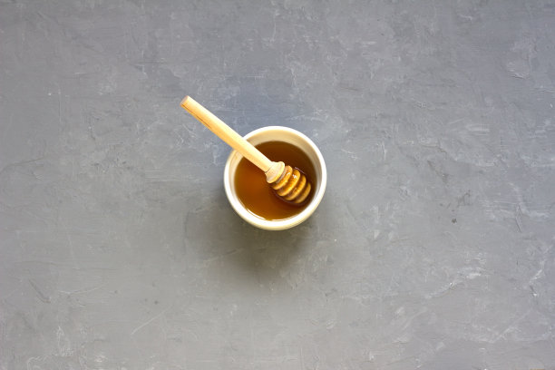 蜂蜜在一个白色的碗和一个木制蜂蜜勺在混凝土背景，自由的空间，俯视图图片下载