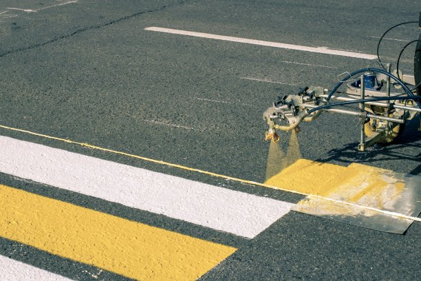 早春，一组工人在新铺的柏油路上使用自动化设备绘制人行横道图片下载