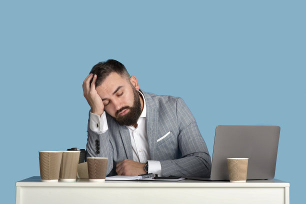 疲惫的商人周围的空咖啡杯睡觉的工作场所，蓝色的工作室背景图片下载