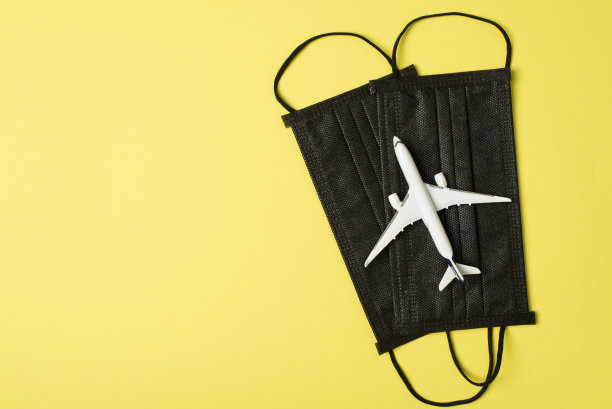 俯视图照片上的飞机模型在两个黑色医疗口罩上孤立的淡黄色背景与copyspace图片下载