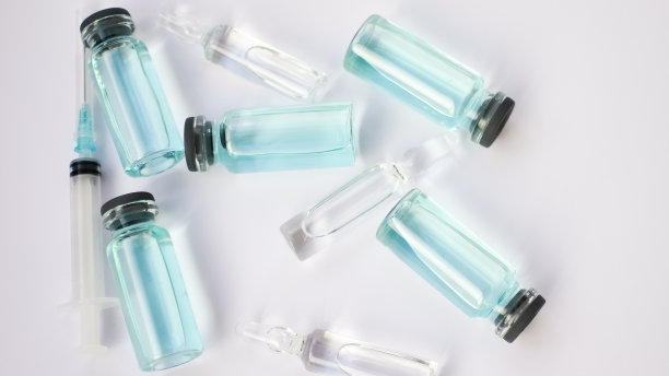 小瓶疫苗，俯视图的玻璃安瓿与透明和蓝色液体躺在白色背景，全球疫苗概念图片下载