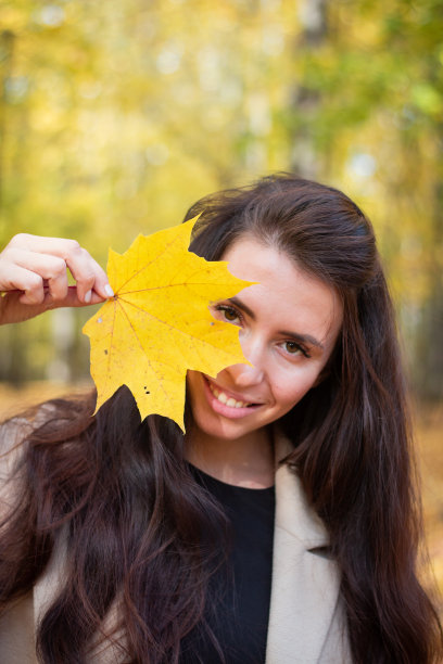 深褐色的女人在秋天的公园和黄色的树叶。关闭计划。微笑的女人。秋天的心情。美丽的黑发。图片下载