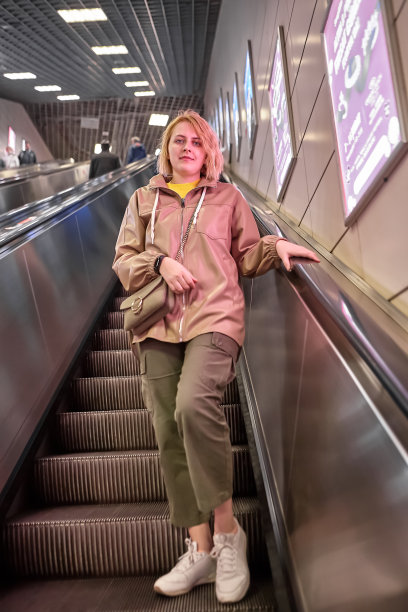 可爱的白人年轻女子站在自动扶梯的台阶上，下到地铁站。图片下载