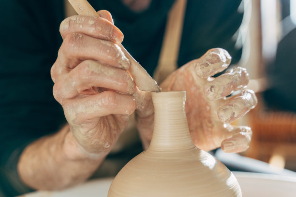 陶工熟练的湿手在陶轮上塑造粘土图片下载