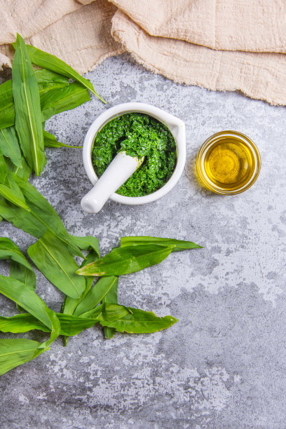 新鲜的熊蒜又称野生蒜或熊蒜香酱，用砂浆和油压碎，放在石头上，混凝土纹理背景和米色厨房桌布上。前视图。垂直的照片。图片下载