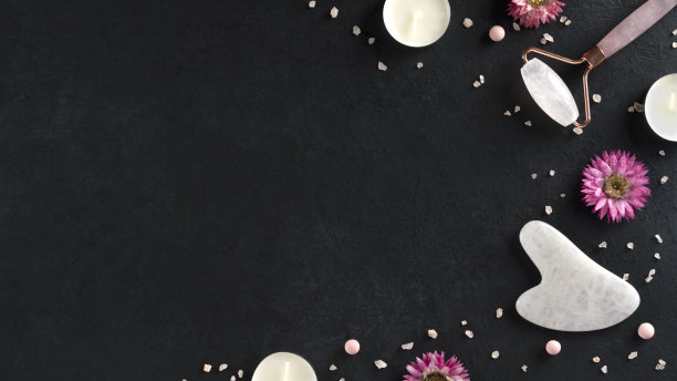 水粉刮刀及玉轮按摩面部。有机化妆品在黑暗的背景与海盐和蜡烛。副本的空间。前视图。图片下载