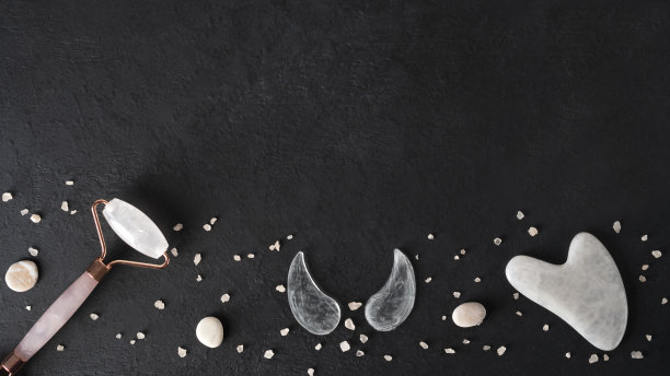 家庭水疗沙龙用水粉画刮刀，面部按摩玉滚轮和眼罩。皮肤护理趋势。提升年轻肌肤。有机化妆品在深色背景与海盐。副本的空间。前视图。图片下载