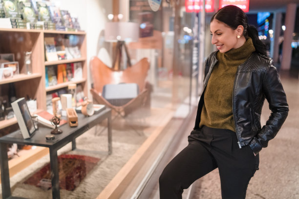 年轻女子晚上站在一家商店的橱窗前。库存图片图片下载